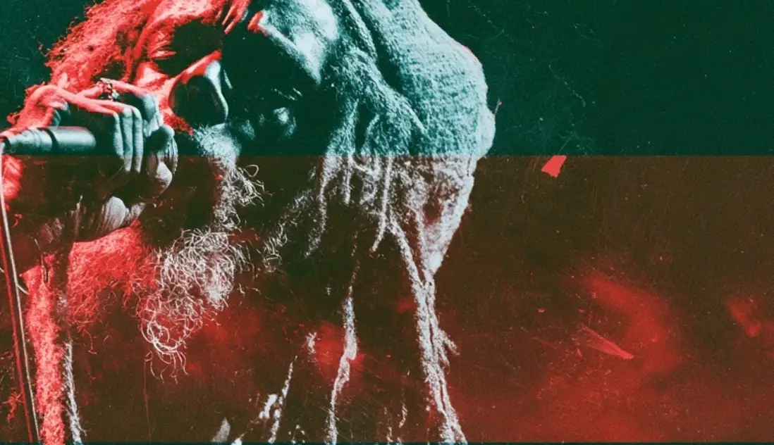 A singer with long locs close to a microphone, head tipped back mid phrase, the picture split into bands of hard red and deep green by the stage lighting.
